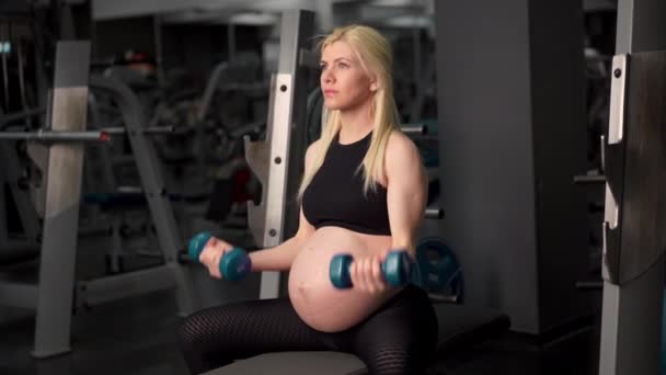 妊娠中の女性持ち上げるダンベルトレーニング二足筋肉にザジム座ってベンチ — ストック動画