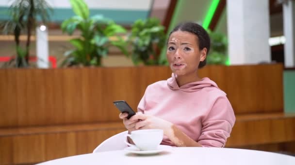 Чорно-афроамериканська жінка з вітиліго проблеми зі шкірою в приміщенні одягнена рожева капуста використовує смартфон. — стокове відео