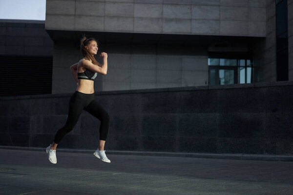 Woman running urban city street background Active sporty caucasian female morning workout Healthy lifestyle concept. Athletic person dressed sportswear do exercises Dark tone mood Corporate building