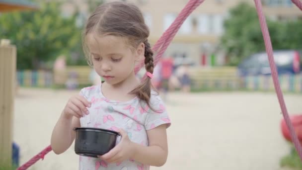 Маленька дівчинка їсть ложку морозива на відкритому повітрі пластикову тарілку Літній день повільний рух — стокове відео