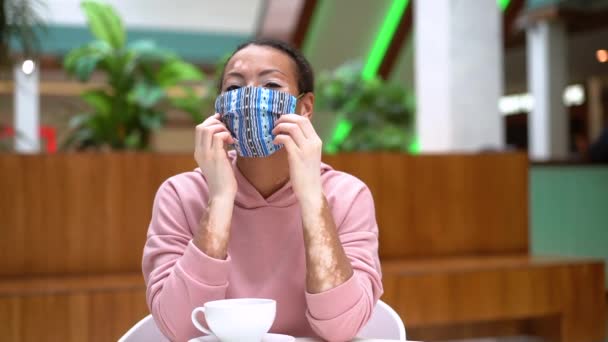 Black African American woman with vitiligo pigmentation skin problem indoor dressed pink hoodie take off protective face mask — Stock Video