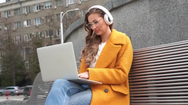 Zakelijke vrouw draagt bril Luister Muziek Hoofdtelefoon Buiten Zitbank Met behulp van laptop Outdoor — Stockvideo
