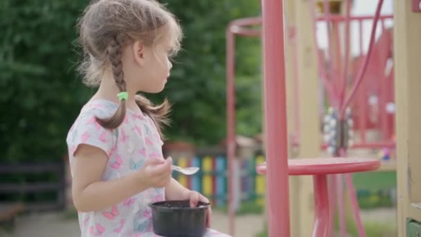 Маленькая девочка ест мороженое ложка на открытом воздухе пластиковой пластины Летний день замедленной съемки — стоковое видео