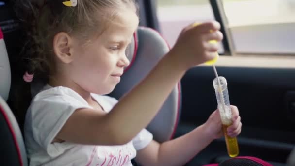 Liten flicka njuter av blåser tvål bubblor under ridning bilbarnstol — Stockvideo