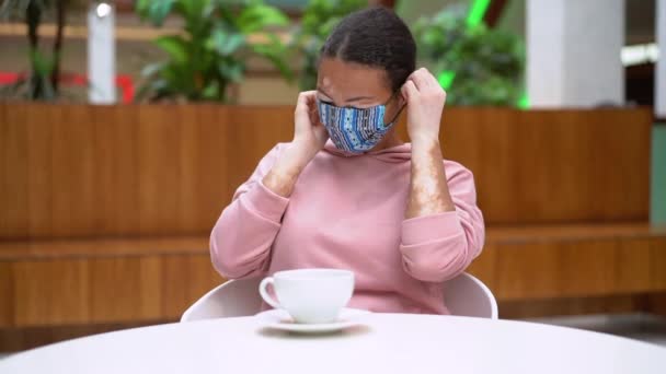 Zwarte Afro-Amerikaanse vrouw met vitiligo pigmentatie huidprobleem indoor gekleed roze hoodie zet op beschermende gezichtsmasker — Stockvideo