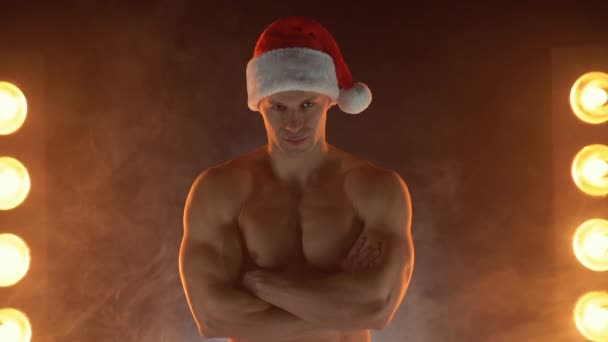 Retrato de homem musculoso usando chapéu de Natal Santa, mãos dobradas sobre fundo fumegante — Vídeo de Stock