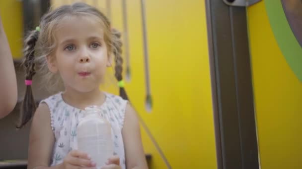 Kleines Mädchen trinkt Wasserflasche nach aktivem Spiel auf Spielplatz — Stockvideo