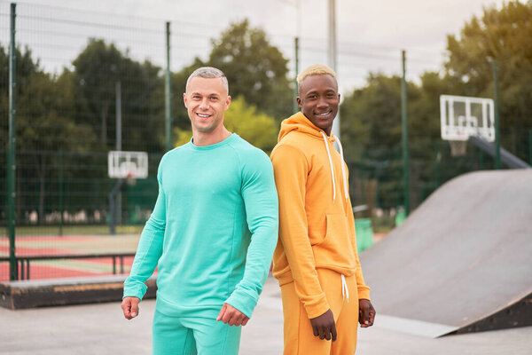 Multi-ethnic friendship Black african-american and caucasian guy friends spending time together on skate park Two multi ethnic student Dressed colorful sportswear.