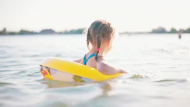 Feliz niña jugando con el agua de mar al aire libre del anillo inflable amarillo en el día caliente del verano. — Vídeo de stock