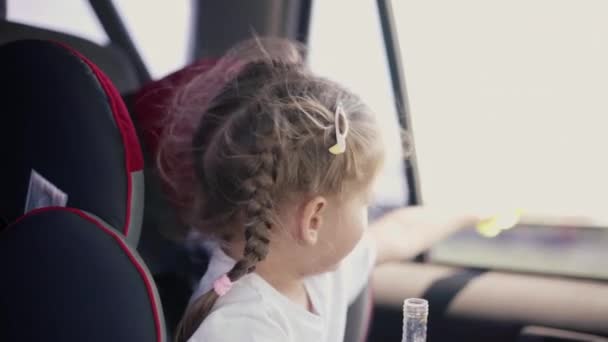 Klein meisje genieten blazen zeepbellen tijdens paardrijden autostoel — Stockvideo