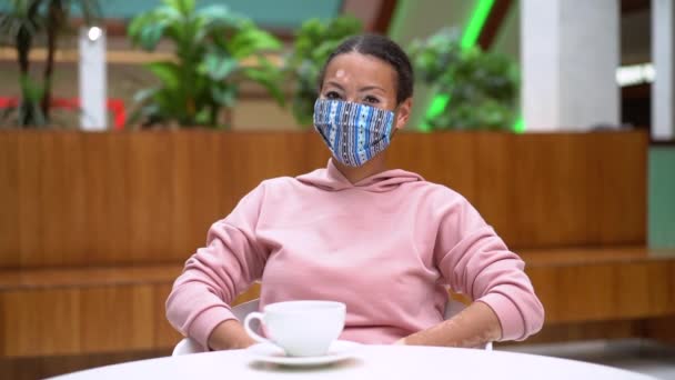 Black African American woman with vitiligo pigmentation skin problem indoor dressed pink hoodie take off protective face mask — Stock Video