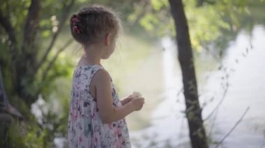 Küçük kız ekmek suyu döktü. Balıkları ve ördekleri besledi. Yaz günü.