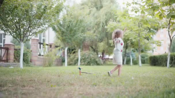 Petite fille caucasienne enfant avoir plaisir saut mains en l'air extérieur arrière-cour journée d'été — Video