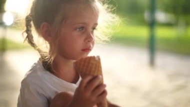 Küçük kız dışarıda dondurma yiyor. Beyaz kadın çocuk waffle külahında beyaz dondurma yalarken eğleniyor. 