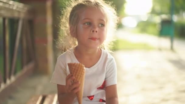 Niña come helado al aire libre. Caucásico niña disfrutar mientras lamer helado blanco en waffle cono — Vídeos de Stock