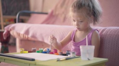 Boyalı fırçayla çizim yapan küçük kız. Oturma odası çocuğu. Su rengini çiziyor.