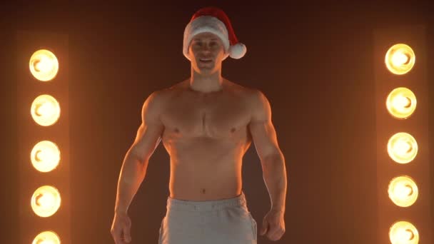 Porträt eines muskulösen Mannes mit Weihnachtsmann-Mütze, der auf verrauchtem Hintergrund steht 
