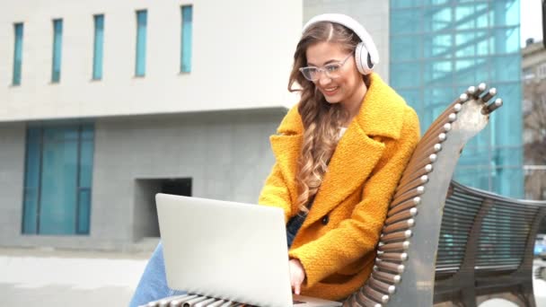 안경을 끼고 있는 사업가가 듣기 음악 헤드폰 실외 문에 앉아 있는 벤치 - 랩탑 옥외 문을 이용함 — 비디오