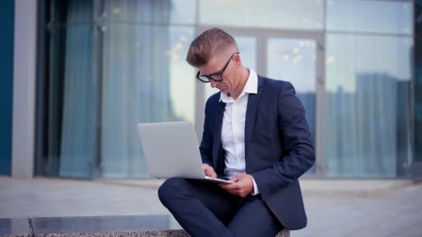 По делам. Бизнесмен с помощью ноутбука сидит на открытом воздухе — стоковое видео