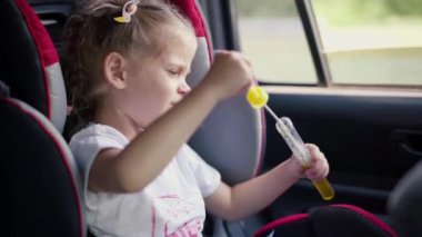 Küçük kız araba koltuğu sırasında sabun köpüğü üflemekten zevk alıyor.