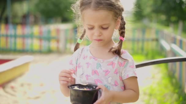 Kleines Mädchen isst Eislöffel Outdoor-Spielplatz Plastikteller Sommertag Zeitlupe — Stockvideo