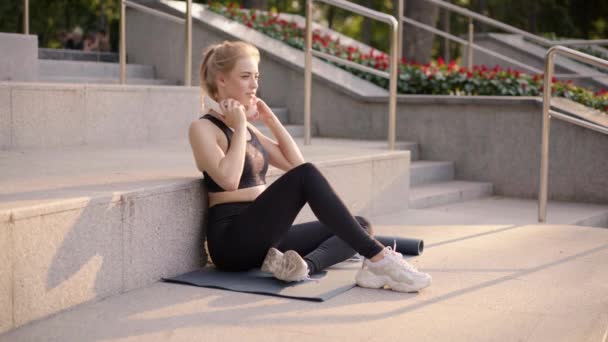 Спорт и фитнес Молодая белая женщина сидя упражнения коврик бетонный пол отдыха после утренней тренировки Открытый летний парк — стоковое видео