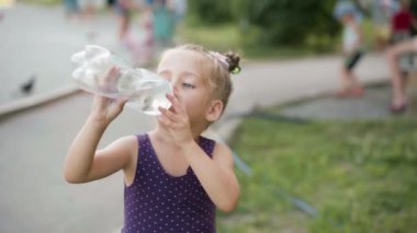 Küçük kız su içiyor. Büyük plastik şişe yaz günü parkı.