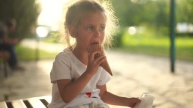 Küçük kız dışarıda dondurma yiyor. Beyaz kadın çocuk waffle külahında beyaz dondurma yalarken eğleniyor. 