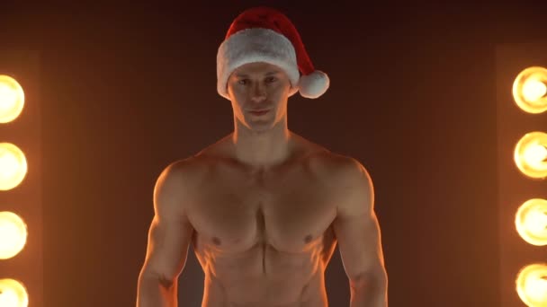 Portret van een gespierde man met kerstmuts, gevouwen handen op een rokerige achtergrond — Stockvideo