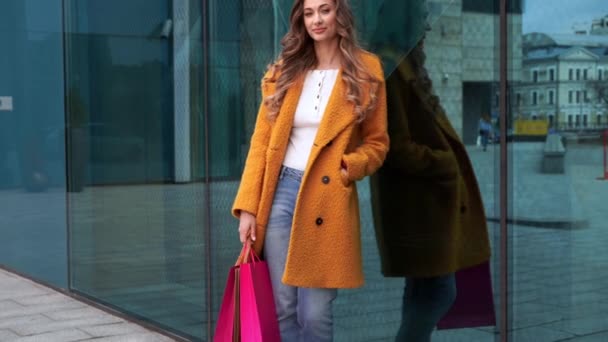 Biznes kobieta z torby na zakupy ubrany żółty płaszcz spacery na zewnątrz korporacyjne tło budynku — Wideo stockowe