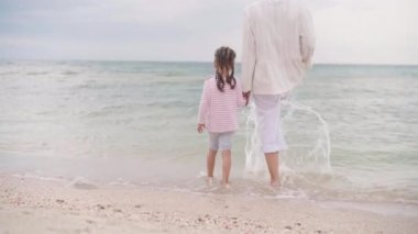 Anne, küçük kızıyla birlikte sahilde mutlu bir ailede yürüyor. Anne, deniz kıyısında küçük bir çocuğun elini tutuyor. Seyahat Eden Yaz Tatili Konsepti 