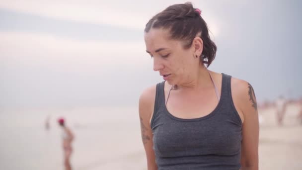 35-jährige Frau mit dunklen Haaren und Tätowierungen im Badeanzug steht am Strand — Stockvideo