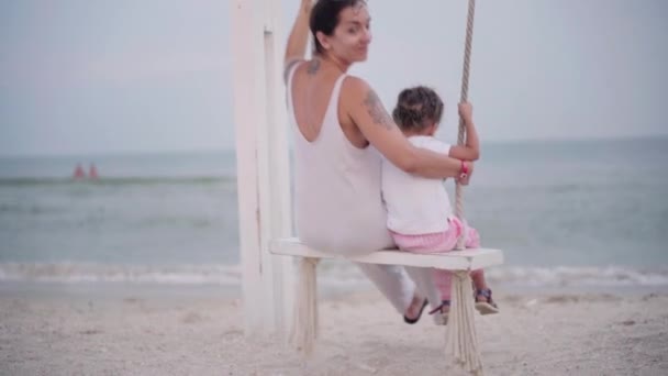 Mutter und Kind schaukeln auf der Strandschaukel mit schöner Familie mit Meerblick im Urlaub — Stockvideo