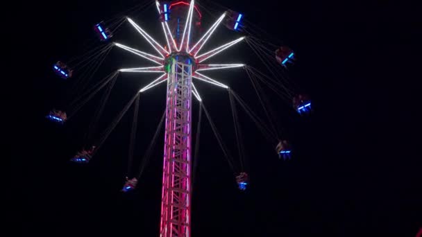 フライングスイングカルーセル遊園地に乗る人々は遊園地で高鎖カルーセルをスイングするときに楽しみを持っています。夜ネオンライト — ストック動画