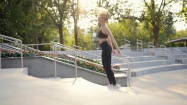 Genç, formda bir kadın yaz günü merdivenlerde zıplayarak çömeliyor. 