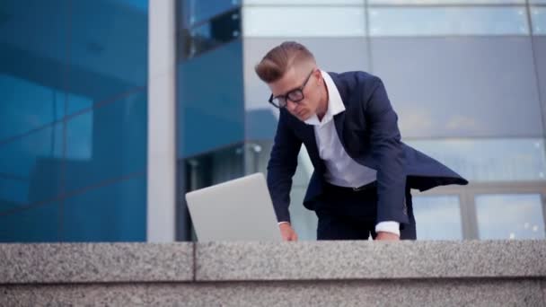 По делам. Бизнесмен с помощью ноутбука сидит на открытом воздухе — стоковое видео