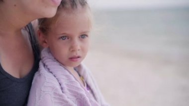 Anne kucaklaşması küçük kızı ısıtıyor. Açık havluyu siliyor. Güneşli bir gün.