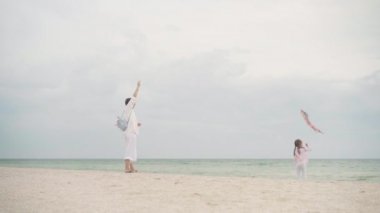 Küçük kızıyla birlikte deniz kıyısında uçurtma oynuyordu. Tek çocuklu mutlu beyaz bir aile deniz kıyısında yaz tatilinde eğleniyordu.