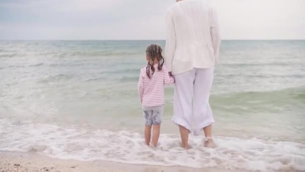 Mutter mit kleiner Tochter am Meer entlang Glückliche Familie am Strand Mutter hält ihr kleines Kind an der Hand, das am Meeresufer entlang geht. Sommerurlaub auf Reisen — Stockvideo