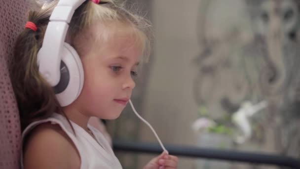 Sofá de niña sentada en auriculares Escuchar música Usar el ordenador portátil Divertirse Inicio Interior Caucásico Femenino Uso del Niño Tecnología Niños modernos Infancia feliz — Vídeo de stock