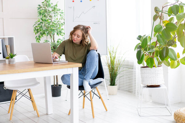 Business woman using laptop sitting desk white office interior with houseplant looking Business people Business person Online, Young and successful Dresed green shirt blue jeans barefoot relaxing 