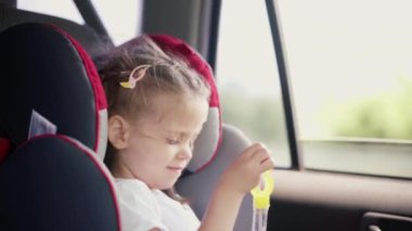 Küçük kız araba koltuğu sırasında sabun köpüğü üflemekten zevk alıyor.