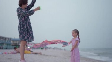 Küçük kızıyla birlikte deniz kıyısında uçurtma oynuyordu. Tek çocuklu mutlu beyaz bir aile deniz kıyısında yaz tatilinde eğleniyordu.