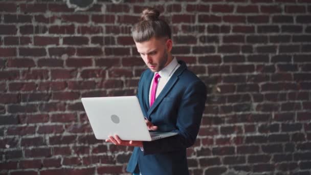 Man standing indoor using laptop dressed suit red brick wall background — Stock Video