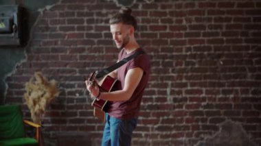 Akustik gitarlı bir adam ileri geri yürür tuğla duvar arkası müzik besteler şarkı söyler, hayatın tadını çıkarır.