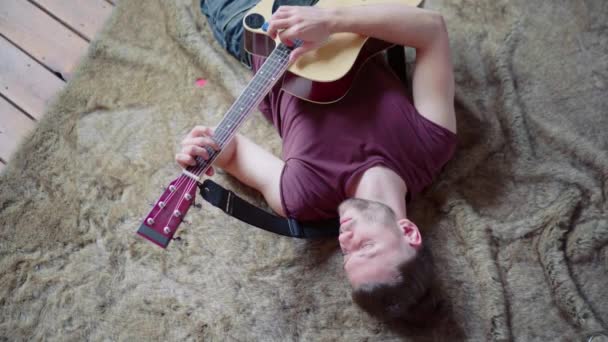 Człowiek z gitarą akustyczną śpiewa i gra na gitarze w pozycji leżącej. Widok góry. Ucieczka od nudy. — Wideo stockowe