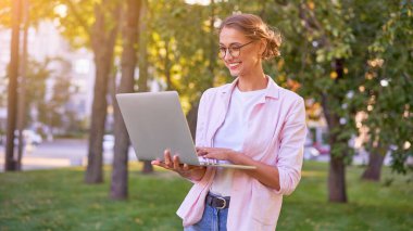 İş kadını yaz parkında dizüstü bilgisayarla uzaktan kumandayla çalışıyor. Açık havada başarılı Avrupalı Kafkasyalı serbest çalışan kadın video çağrı öğretmenini çevrimiçi derslere çalıştırdı 