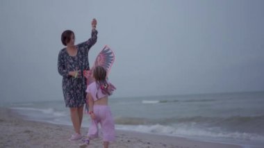 Küçük kızıyla birlikte deniz kıyısında uçurtma oynuyordu. Tek çocuklu mutlu beyaz bir aile deniz kıyısında yaz tatilinde eğleniyordu.