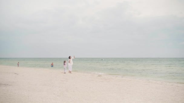 Küçük kızıyla birlikte deniz kıyısında uçurtma oynuyordu. Tek çocuklu mutlu beyaz bir aile deniz kıyısında yaz tatilinde eğleniyordu. — Stok video