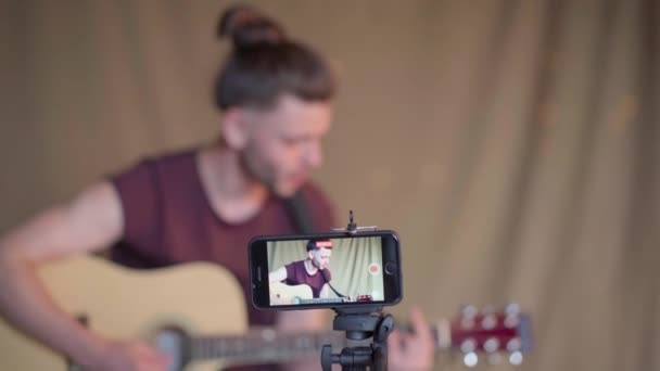 Homem gravando aulas de guitarra para estudantes. Cursos de guitarra online. Conceito de ensino à distância Foco na tela do dispositivo — Vídeo de Stock